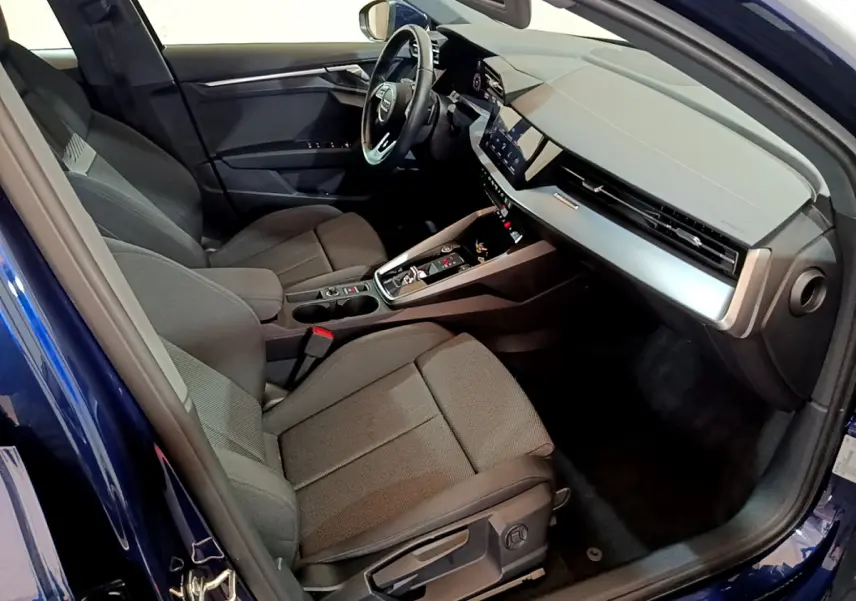 Intérieur de l'Audi A3 bleu 2023 vu côté conducteur, sièges tissu gris et tableau de bord moderne avec écran tactile.