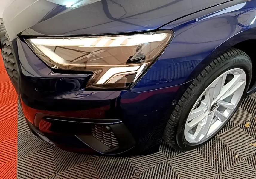 Gros plan sur l'avant droit bleu d'une Audi A3 35 TFSI 150 MHEV avec phare LED et jante argentée.
