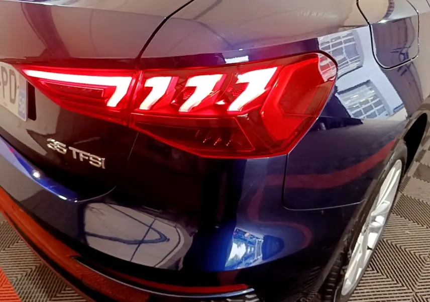 Gros plan sur le feu arrière droit rouge vif d'une Audi A3 35 TFSI bleu foncé, avec logo et jante visible.