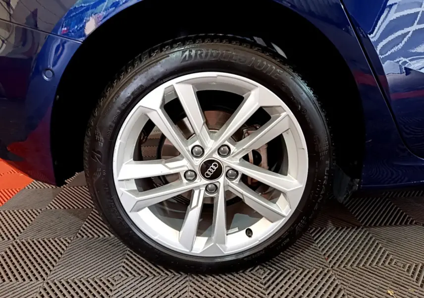 Gros plan sur la roue avant gauche d’une Audi A3 bleu 2023 avec jante alliage argentée et logo Audi central.