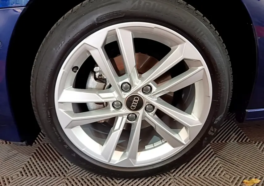 Gros plan sur la jante argentée d'une Audi A3 bleu 2023, mettant en valeur le logo Audi au centre.