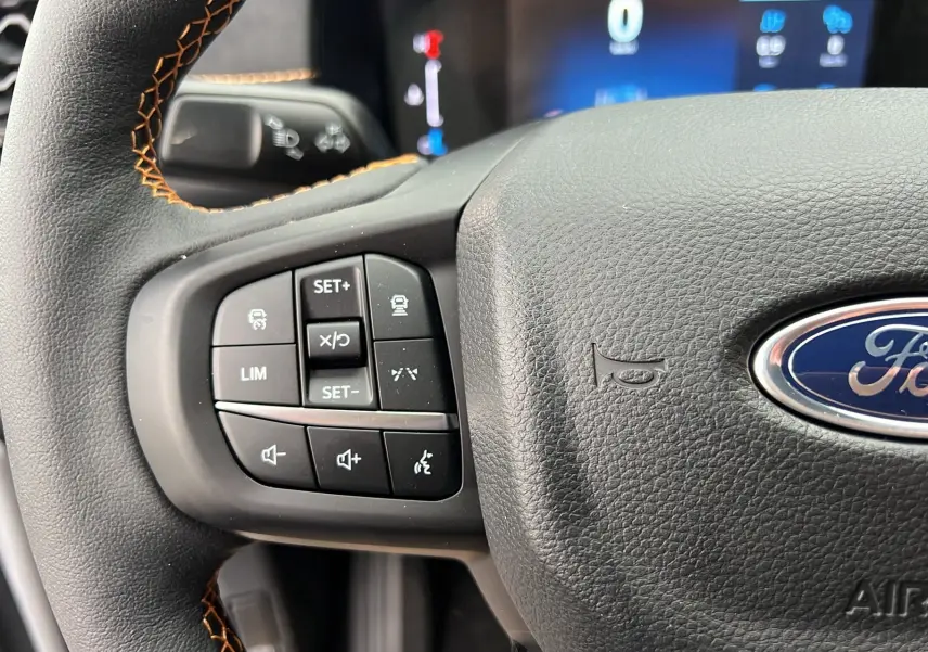 Gros plan sur le volant cuir noir avec surpiqûres orange du Ford Ranger gris iconic, boutons multifonctions visibles.
