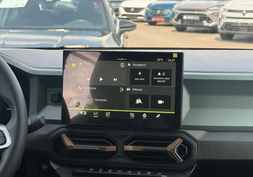 Vue intérieure centrée sur l'écran tactile du tableau de bord du Dacia Duster 2026, avec commandes clim et volant partiel visible.