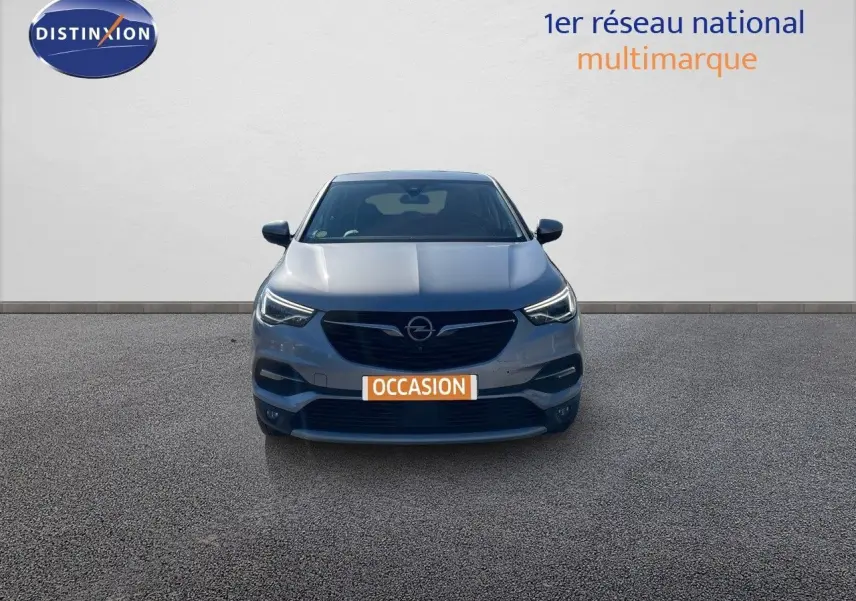 Vue de face d'un Opel Grandland X gris quartz métal avec phares allumés sur fond neutre.