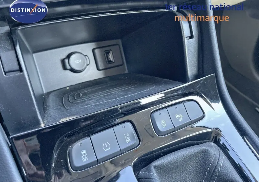 Gros plan sur la console centrale noire de l’Opel Grandland X gris quartz, montrant les boutons de contrôle et prise 12V.