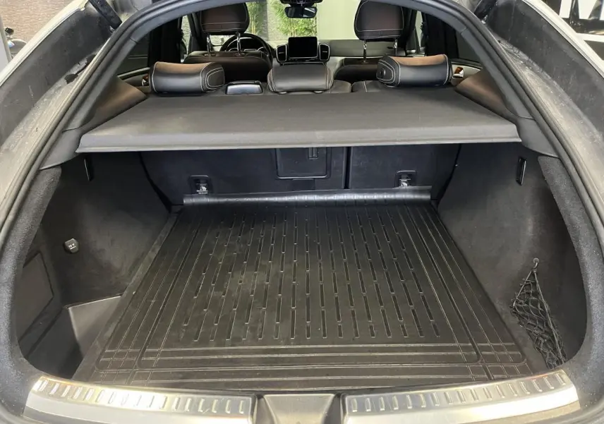 Coffre ouvert vu de l'arrière d'un Mercedes GLE Coupé blanc avec cache-bagages et tapis de protection noir.