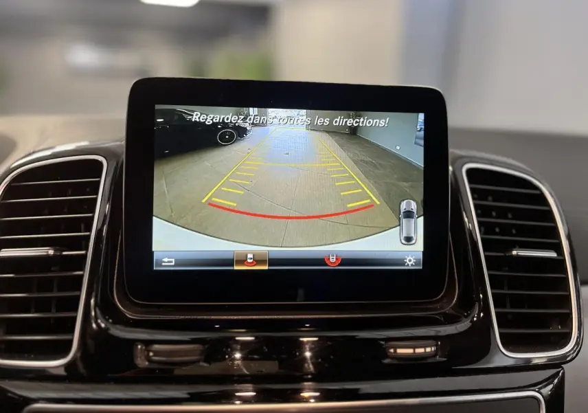 Écran central du Mercedes GLE Coupé blanc 2016 affichant la caméra de recul avec lignes de guidage en intérieur.