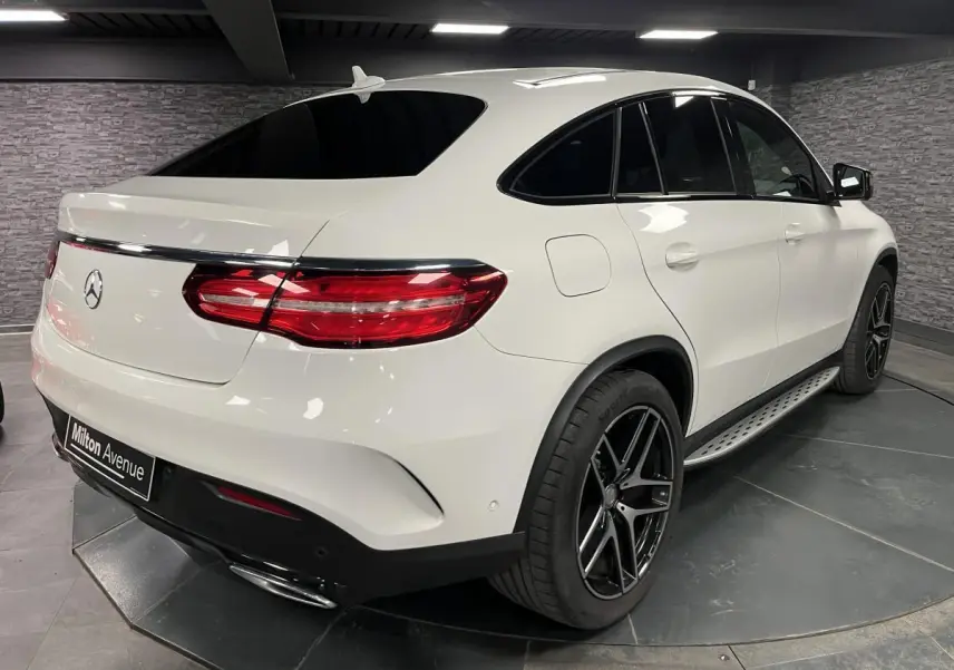 Vue 3/4 arrière droite d'un Mercedes GLE Coupé 350 d blanc avec jantes AMG noires et toit panoramique.