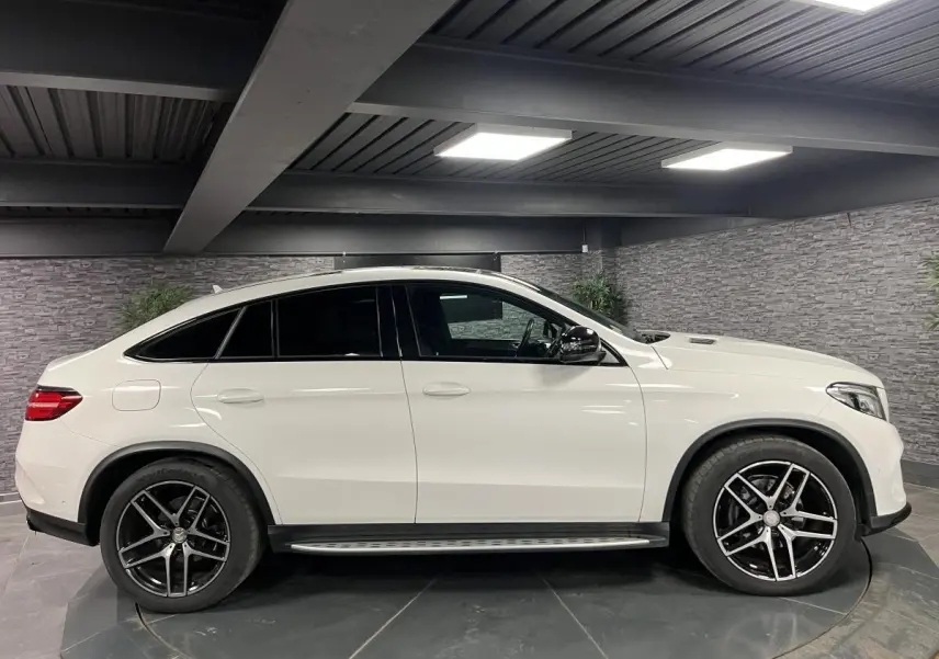 Profil côté gauche d'un Mercedes GLE Coupé 350 d blanc avec jantes AMG noires et vitres teintées dans un garage.