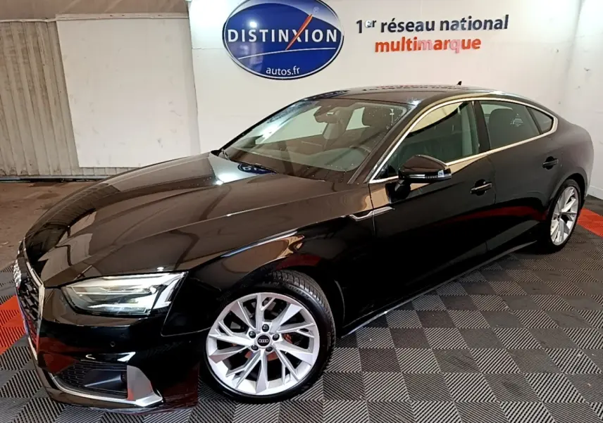 Audi A5 noir vue 3/4 avant droit dans un showroom avec jantes argentées et phares LED allumés.