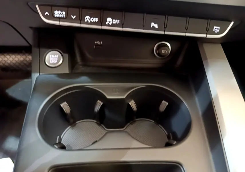 Gros plan sur la console centrale noire de l'Audi A5 35 TFSI avec boutons de commande et porte-gobelets.