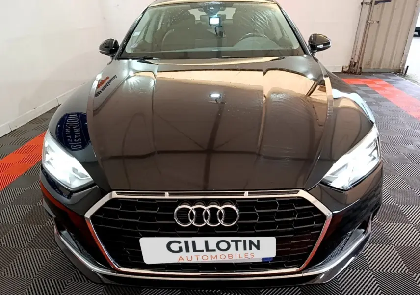 Vue avant d'une Audi A5 noire avec phares LED allumés et calandre hexagonale chromée dans un garage.