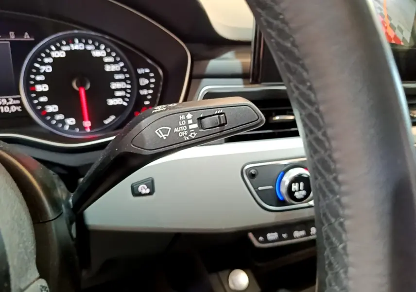 Gros plan sur la manette d’essuie-glace et le tableau de bord gris clair de l’Audi A5 noire, avec volant en cuir visible.