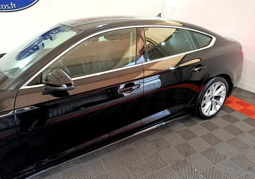 Profil côté gauche d'une Audi A5 noire brillante, mettant en valeur ses lignes fluides et ses jantes argentées.