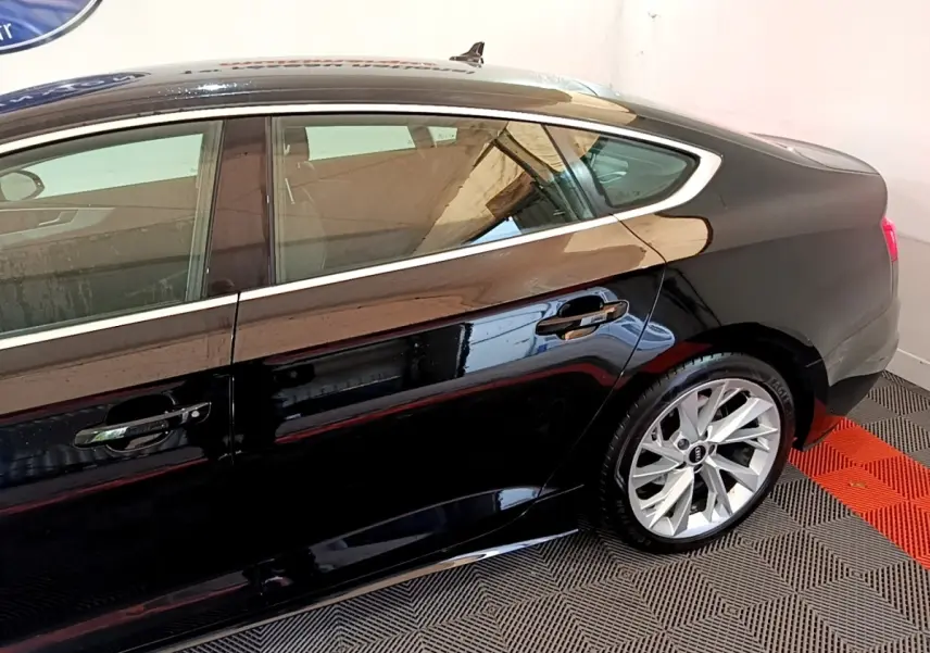 Profil côté gauche de l'Audi A5 noire 2021 avec jantes alliage et ligne de toit sportive dans un garage.