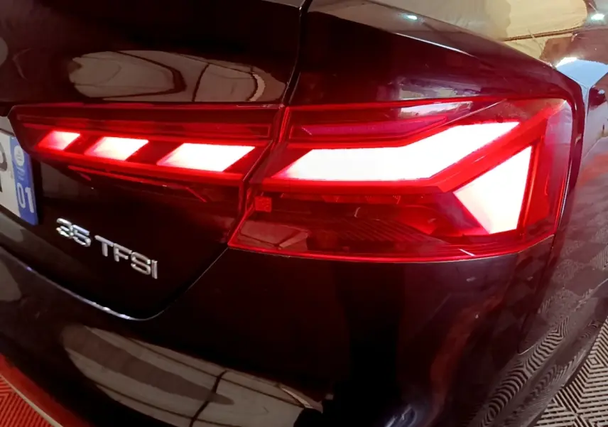 Feu arrière droit allumé d'une Audi A5 35 TFSI noire, vue rapprochée sur le logo et la carrosserie brillante.
