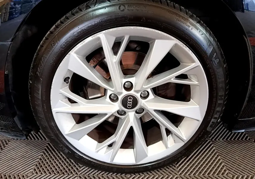Gros plan sur la jante argentée d'une Audi A5 noire, mettant en valeur le logo Audi au centre du pneu Michelin.