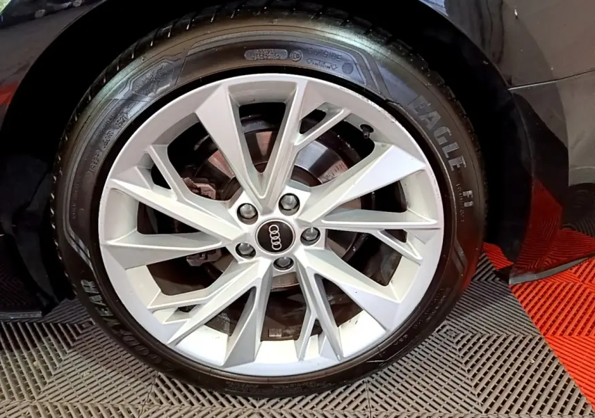 Gros plan sur la jante argentée à dix branches de l'Audi A5 noire, avec pneu Goodyear Eagle visible au sol.