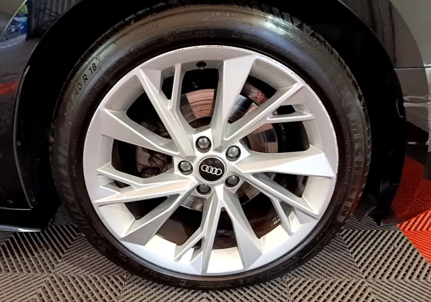 Gros plan sur la roue avant droite d'une Audi A5 noire, mettant en valeur la jante argentée à design étoilé.