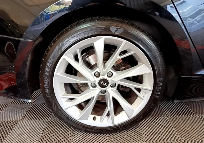 Gros plan sur la roue avant droite noire d'une Audi A5 35 TFSI 150 S TRONIC 7 BUSI LINE avec jante argentée multi-branches.