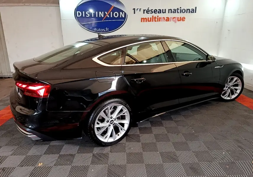 Audi A5 noire vue de 3/4 arrière droit, avec feux LED allumés et jantes argentées dans un showroom.