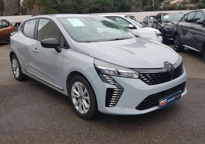 Renault Clio gris clair vue 3/4 avant droit, avec signature lumineuse LED distinctive et calandre noire.