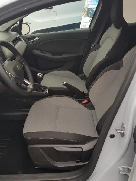 Vue intérieure côté conducteur de la Renault Clio gris 2025, montrant les sièges tissu bicolore et la boîte manuelle.
