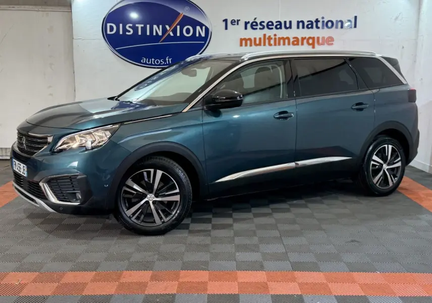 Vue latérale droite d'un Peugeot 5008 bleu métallisé, avec jantes alliage et toit chromé dans un showroom.