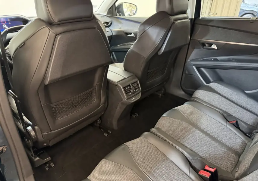 Vue intérieure arrière côté droit du Peugeot 5008 bleu, montrant les sièges tissu et cuir et les dossiers des sièges avant en cuir noir.