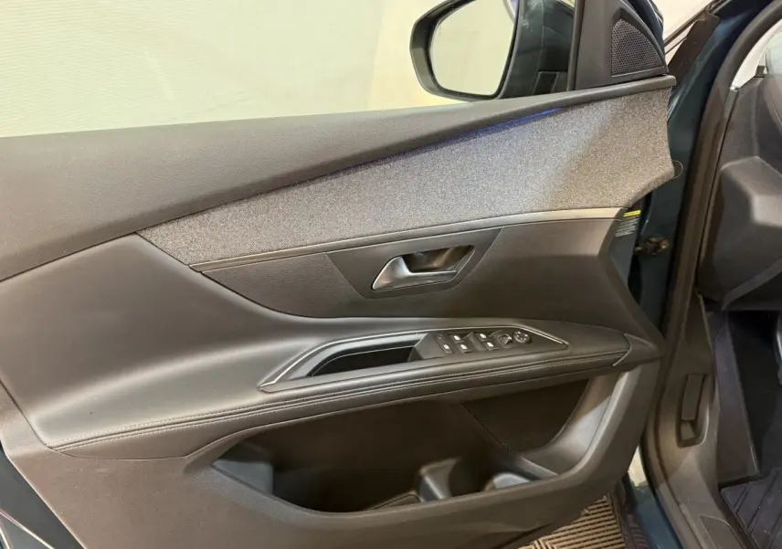Vue intérieure côté gauche de la porte avant d’un Peugeot 5008 bleu, avec commandes électriques et garniture noire.