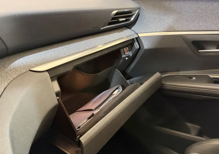 Vue intérieure côté passager du Peugeot 5008 bleu 2019, boîte manuelle, montrant la boîte à gants ouverte avec un document à l'intérieur.