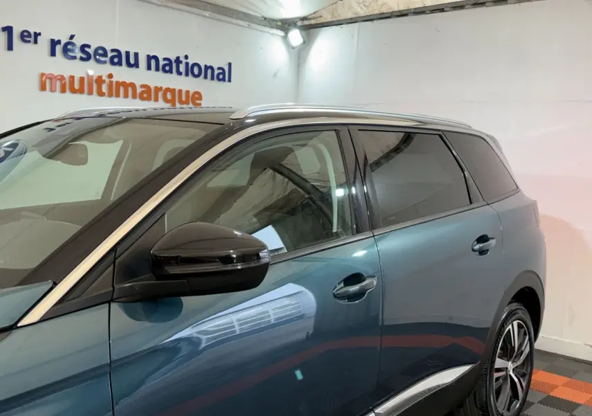 Vue latérale côté gauche d'un Peugeot 5008 bleu avec rétroviseur noir et vitres teintées dans un garage.