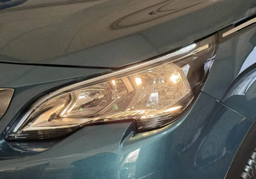 Gros plan sur le phare avant droit allumé d’un Peugeot 5008 bleu métallisé, version Puretech 130 S&S Allure.