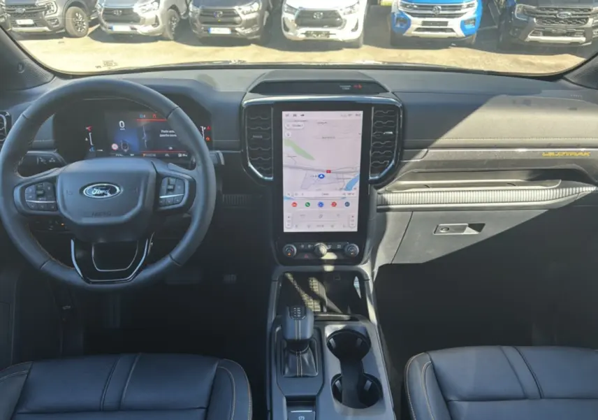 Vue intérieure avant du Ford Ranger Wildtrak 2025, tableau de bord noir avec écran tactile vertical et volant multifonctions.