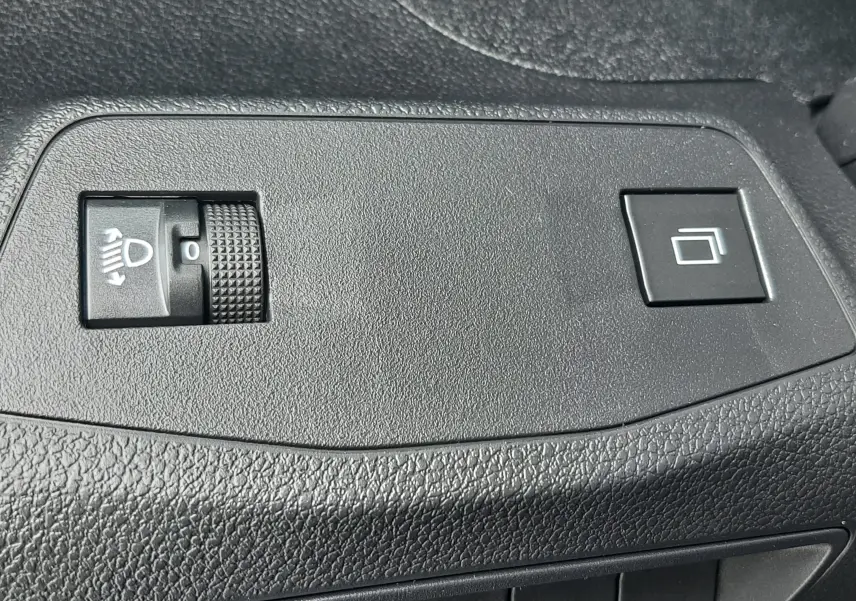 Gros plan sur les commandes noires du tableau de bord intérieur du Peugeot Rifter bleu Kiama, boutons de réglage des phares et fonction tactile.