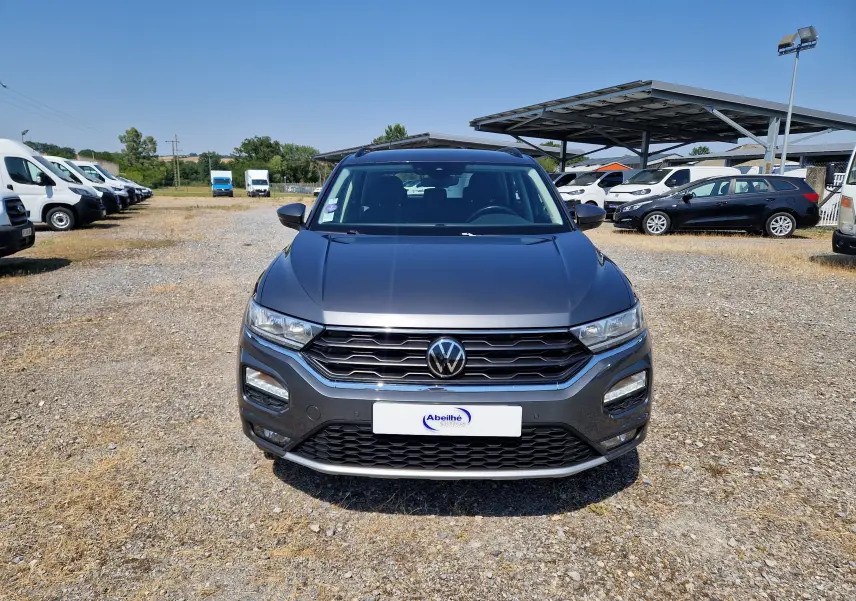 Volkswagen T-Roc 1.0 TSI gris foncé métal, vue de face sur un parking extérieur ensoleillé.