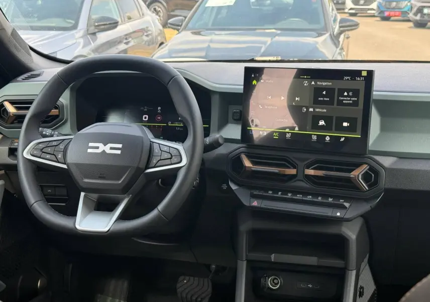 Vue intérieure du tableau de bord et volant multifonction du Dacia Duster 2026 avec écran tactile central et aérateurs hexagonaux.