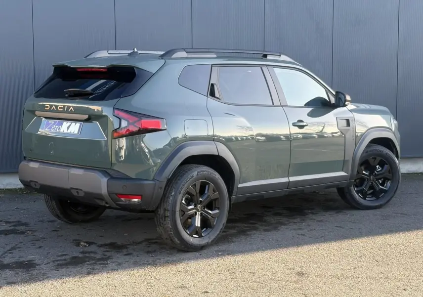 Vue 3/4 arrière droite du Dacia Duster 2026 kaki Lichen avec jantes alliage noires et barres de toit grises.