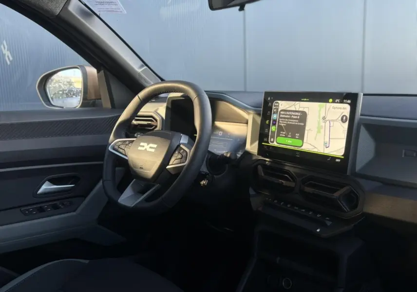 Vue intérieure côté conducteur du Dacia Duster 2026, avec tableau de bord digital et écran tactile central affichant la navigation.