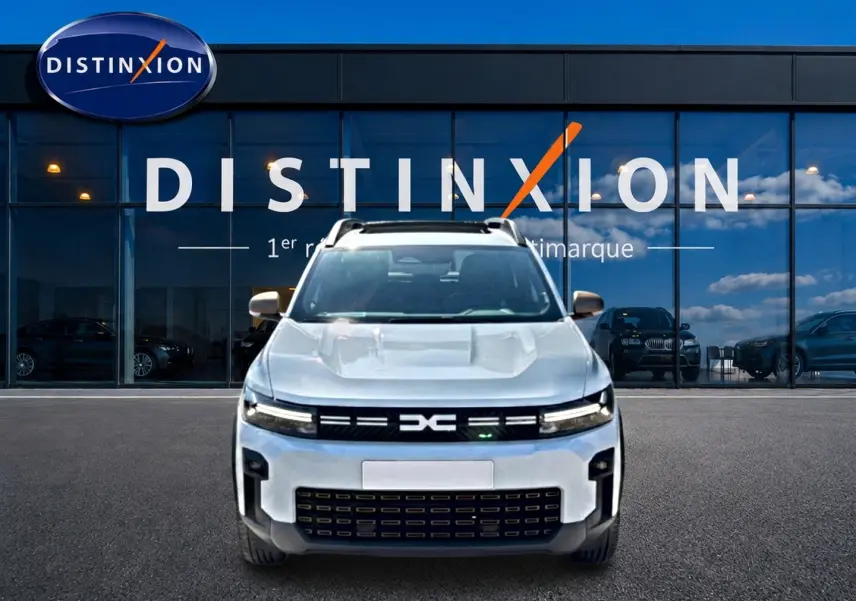 Vue avant d'un Dacia Bigster blanc 2026 avec calandre noire et toit ouvrant panoramique, devant une vitrine Distinxion.