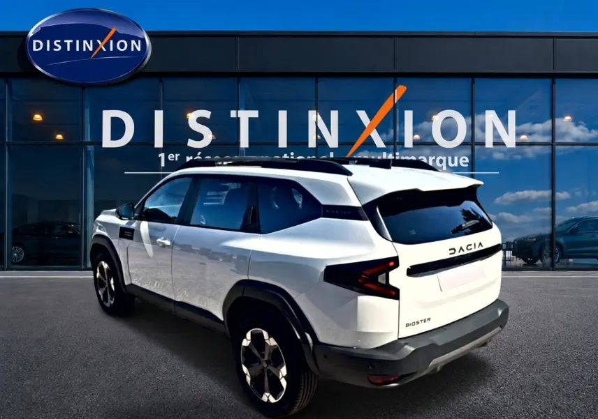 Vue 3/4 arrière droite d'un Dacia Bigster blanc avec toit noir et jantes alu devant une vitrine Distinxion.