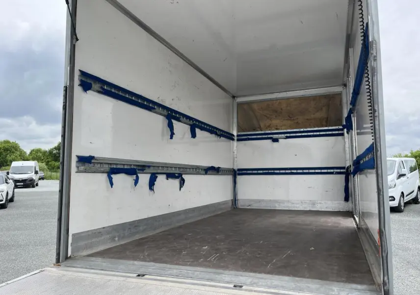 Intérieur du fourgon blanc FIAT Ducato Maxi Business 3.5 vu de l'arrière, montrant l'espace de chargement vide et ses rails bleus.