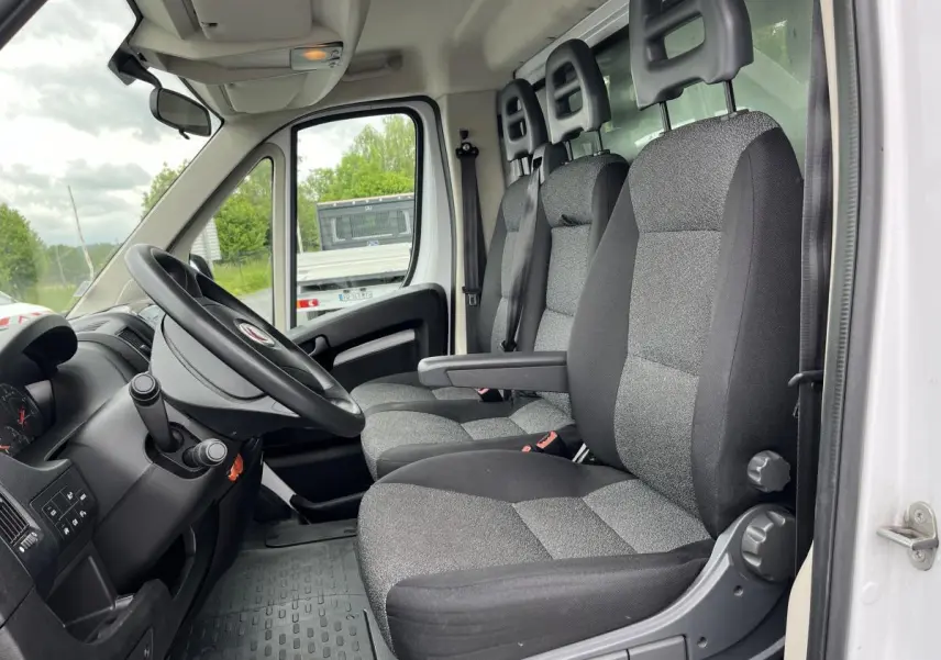 Intérieur côté conducteur du Fiat Ducato blanc, montrant les sièges avant gris et le volant noir.