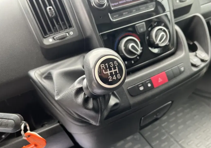 Gros plan sur le levier de vitesses manuel du Fiat Ducato Fourgon blanc, avec tableau de bord et commandes climatisation visibles.