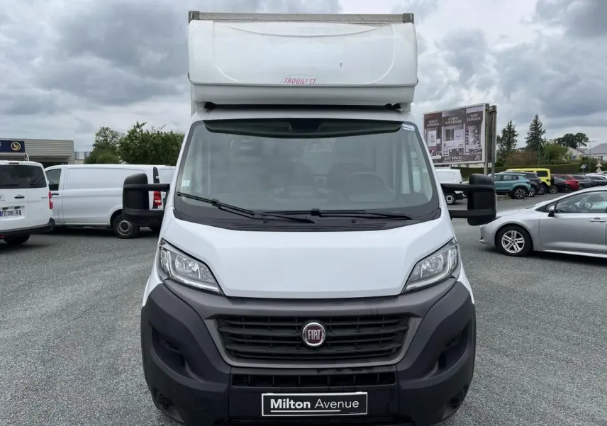 Vue frontale d'un FIAT Ducato Fourgon Maxi Business blanc avec capucine et pare-chocs noirs sur parking.