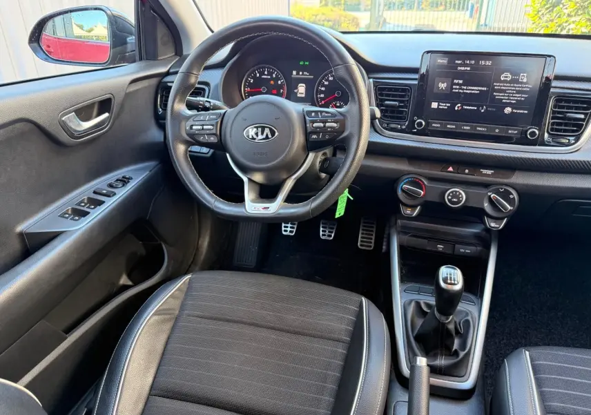 Vue intérieure côté conducteur de la KIA RIO rouge grenadine 2022, volant multifonction et boîte manuelle visibles.