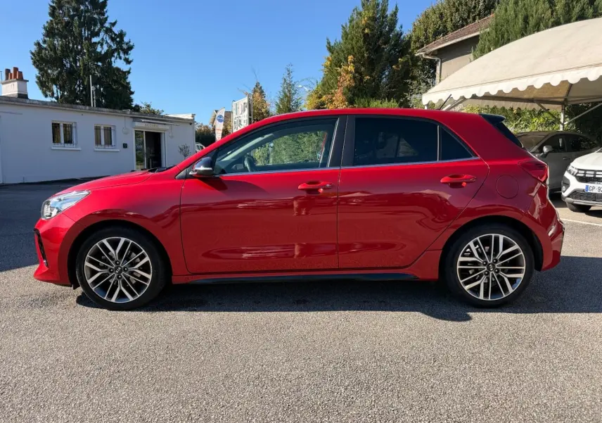 Profil côté gauche d'une KIA RIO rouge grenadine 2022 en finition GT-LINE, avec jantes alliage et lignes dynamiques.