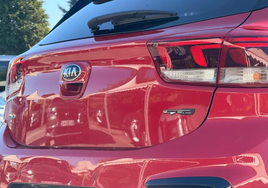 Vue arrière droite d'une KIA RIO rouge grenadine GT-Line 2022 avec logo et feux arrière distinctifs.
