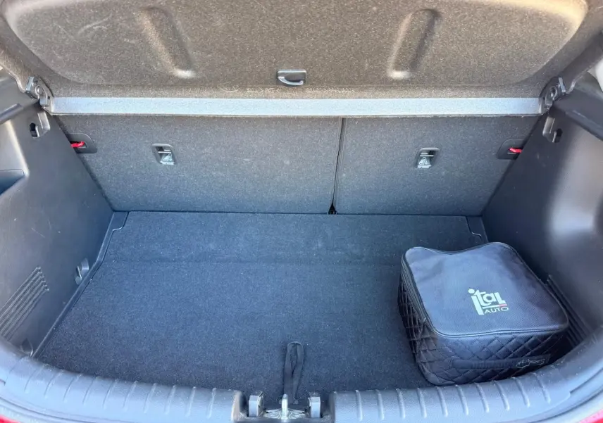 Coffre ouvert d'une KIA RIO rouge grenadine 2022, montrant un espace de rangement propre avec une trousse noire Ital Auto.