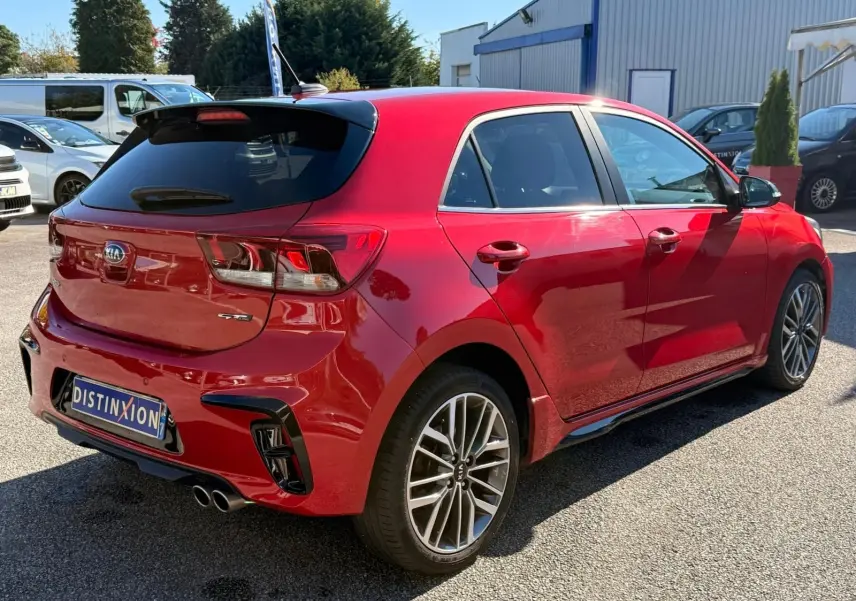 KIA Rio GT-Line rouge grenadine vue 3/4 arrière droit, jantes alliage et double sortie d’échappement visibles.